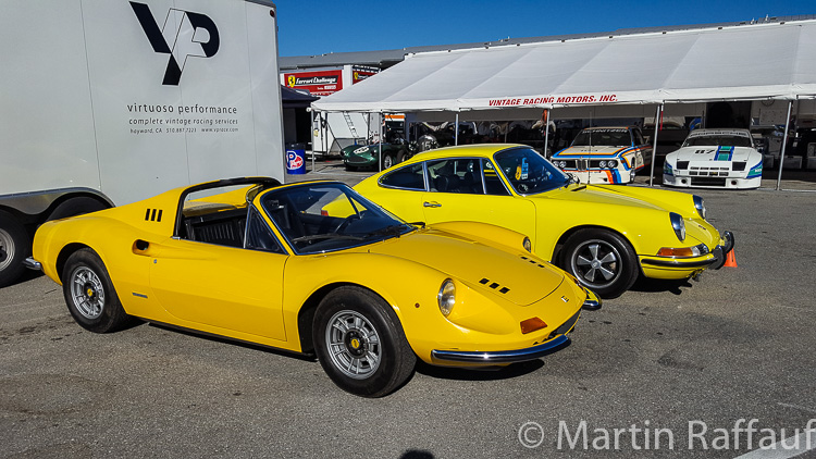 Two pristine yellow cars in the paddock. A Ferrari Dino and a 1972 Porsche 911 T 2.2