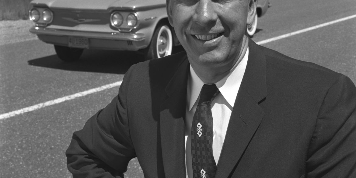 Black and white photo of Ed Cole standing in front of Chevrolet Corvair