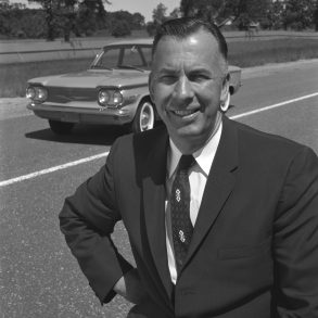 Black and white photo of Ed Cole standing in front of Chevrolet Corvair