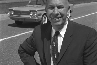 Black and white photo of Ed Cole standing in front of Chevrolet Corvair