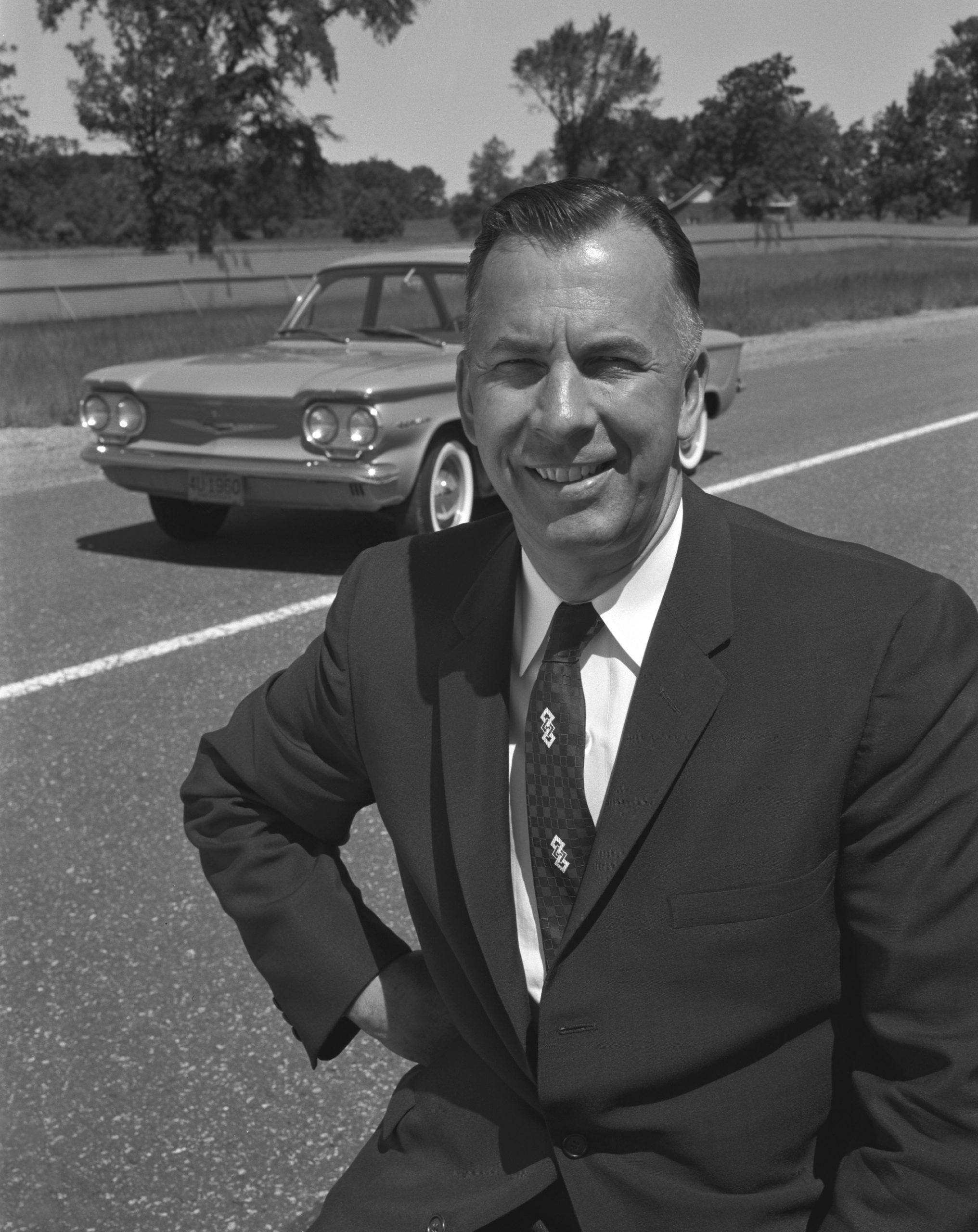 Black and white photo of Ed Cole standing in front of Chevrolet Corvair