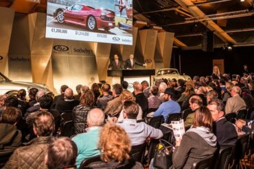 Crowd of people bidding on Porsches at auction