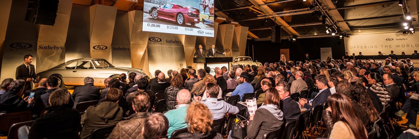 Crowd of people bidding on Porsches at auction