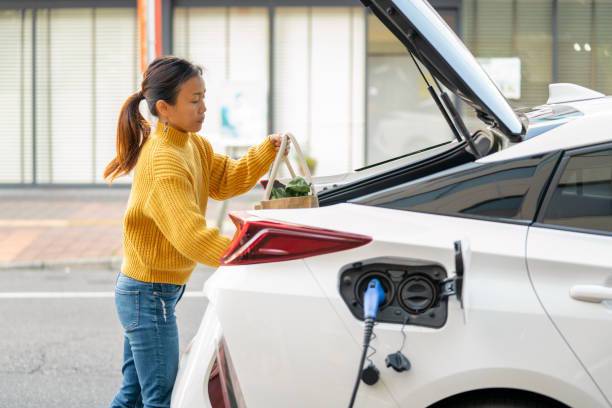 Woman loading groceries into trunk of electric car while it charges