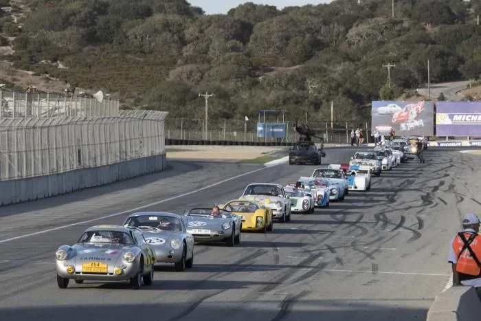 A variety of Porsche race cars from the 50s through the 90s during a parade lap