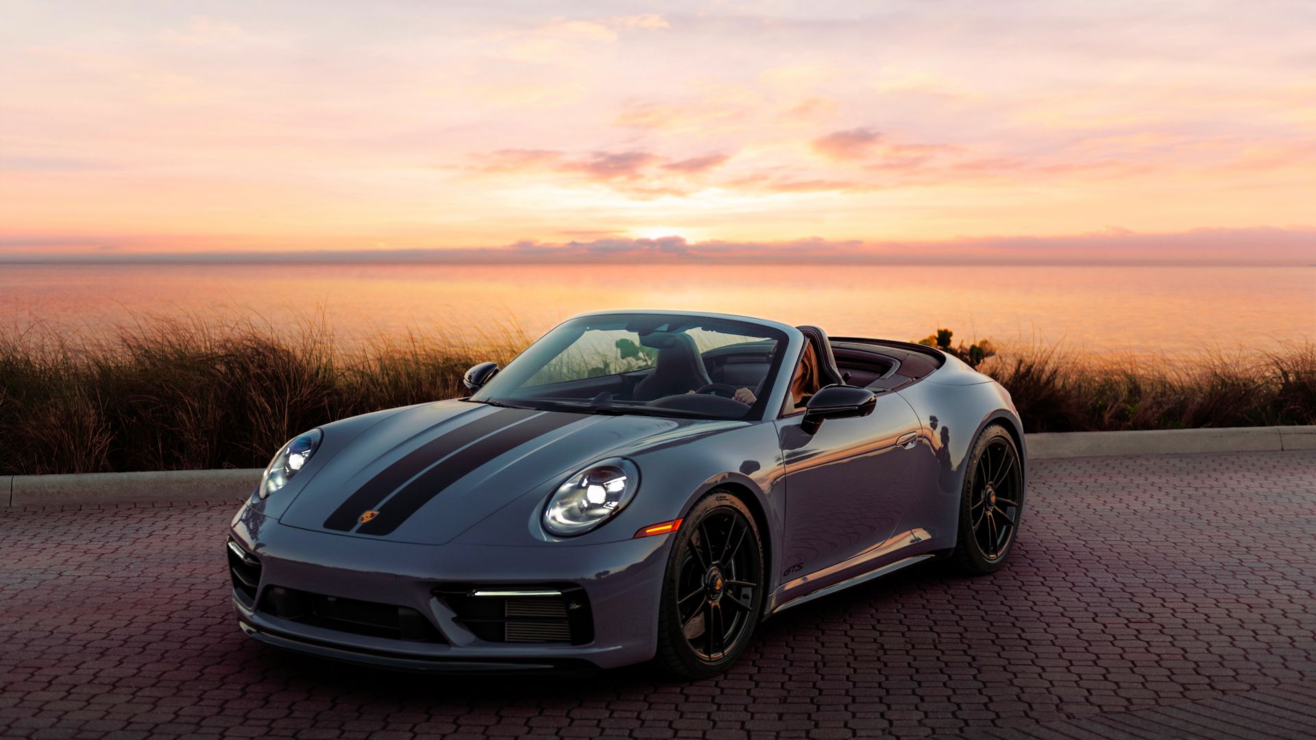 3/4 front view of a gray 911 Carrera 4 GTS Cabriolet with sunset background