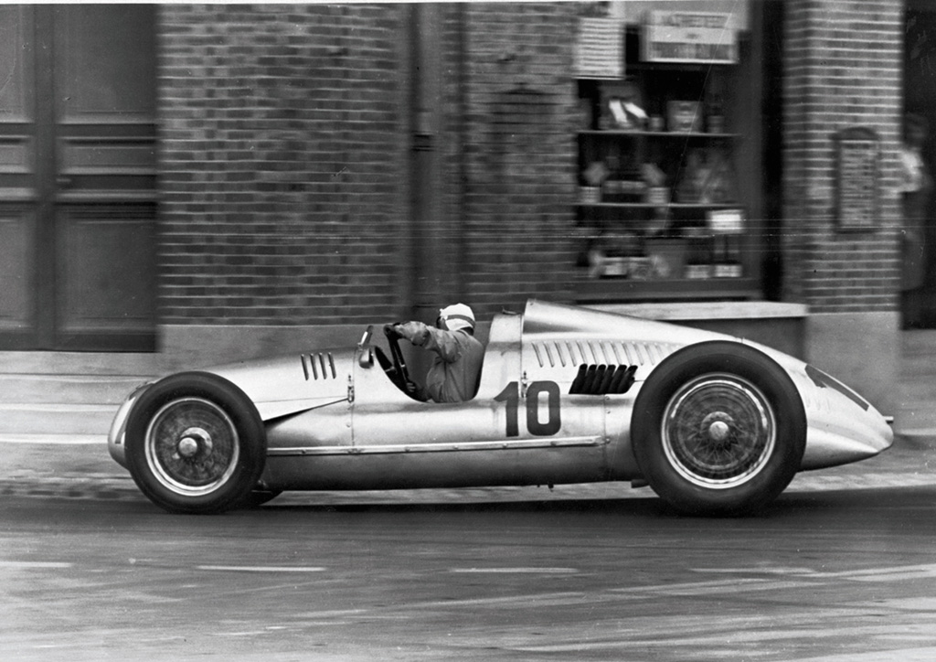 The Auto Union Type D was developed for the new 1938 Grand Prix regulations, which limited supercharged engines to three liters and brought the earlier V16 era to an end. Powered by a supercharged V12 producing more than 400 horsepower, it retained the mid-engine architecture established under Ferdinand Porsche while reflecting the later design leadership of Robert Eberan von Eberhorst. With Tazio Nuvolari at the wheel, the Type D delivered major victories and proved that Auto Union’s unconventional racing formula could survive a dramatic change in regulation.