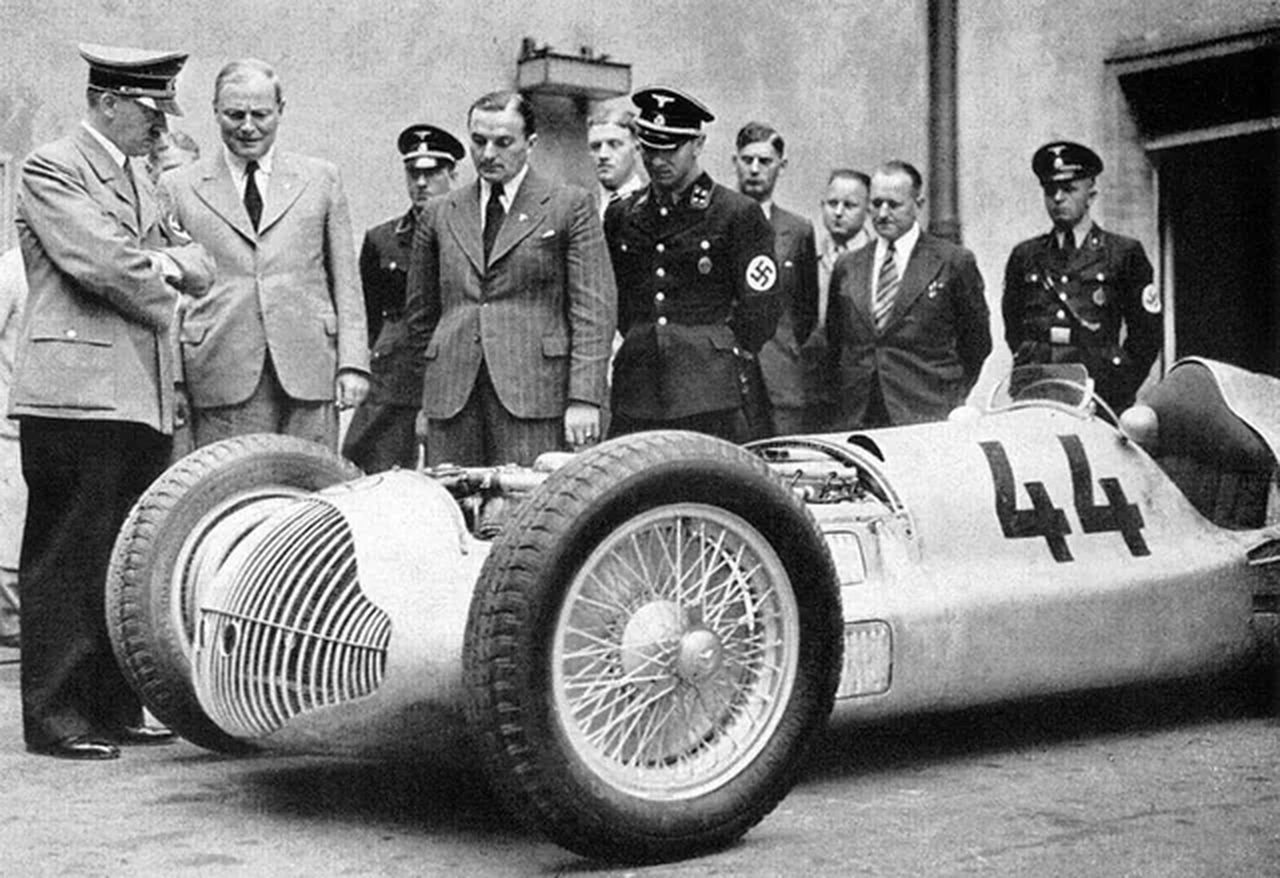 Seen here examining the Mercedes-Benz W154, Adolf Hitler understood Grand Prix racing as far more than sport. Victories by German cars and drivers could be used to present the nation as technologically advanced, disciplined, and superior—reinforcing the regime’s broader propaganda about German strength in engineering, industry, and society. The W154 became one of the clearest examples of how motorsport was transformed into both a technical contest and an instrument of political power.