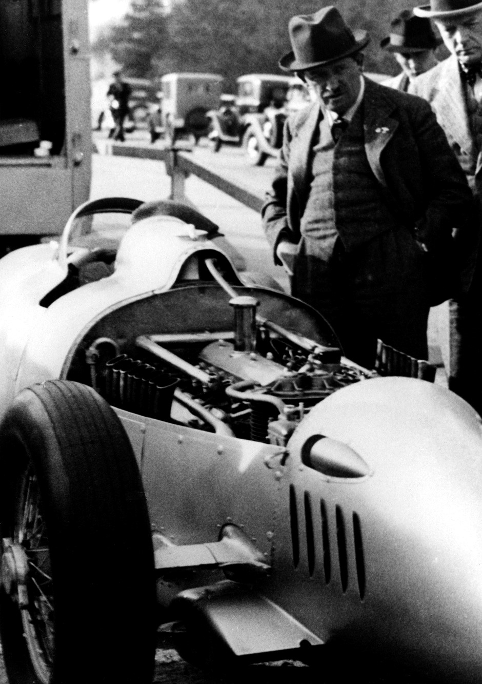 This period photograph captures the P-Wagen during its development, the radical Grand Prix concept created under Ferdinand Porsche’s direction. Rather than placing the engine ahead of the driver, Porsche positioned it behind the cockpit and ahead of the rear axle, creating what would now be recognized as a mid-engine layout. The arrangement promised improved traction and more favorable weight distribution, but it also produced handling characteristics that demanded considerable skill from the driver. It was a dramatic break from convention—and the foundation of the Auto Union racers that followed.