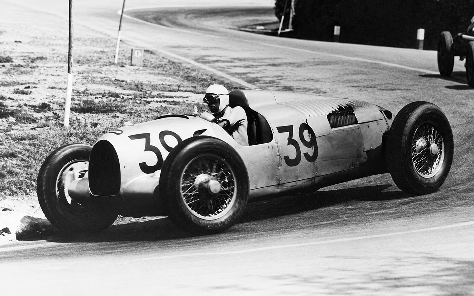 Seen here at the wheel of the No. 39 Auto Union Type B, Achille Varzi brought precision, restraint, and years of Grand Prix experience to Porsche’s unconventional rear-engined racer. Accustomed to front-engined machinery, Varzi had to retrain many of the instincts that had shaped his career, yet he still delivered important victories for Auto Union. His success demonstrated that the Type B could be mastered by an established Grand Prix driver—even if doing so required an entirely different approach.