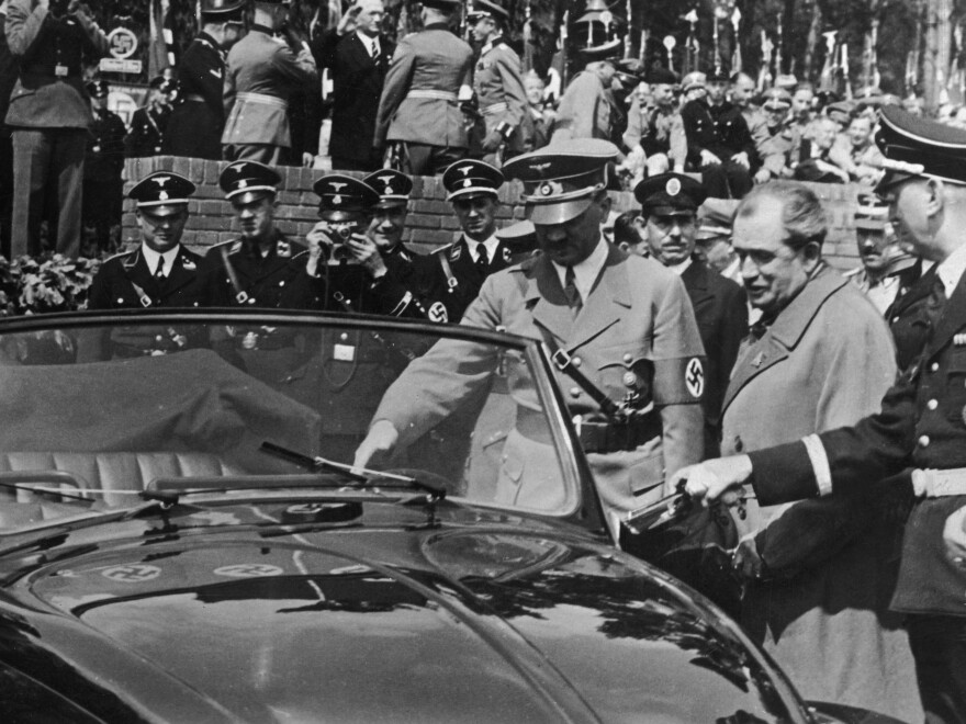 This image captures more than a meeting between Ferdinand Porsche and Adolf Hitler; it shows how thoroughly the Volkswagen project had become embedded in the regime’s political theater. Porsche’s status as an SS officer placed him inside the system of honors, influence, and personal loyalty that surrounded Hitler, while public appearances such as this helped present the automobile as a triumph of National Socialist planning rather than the work of an independent engineering office. That association elevated Porsche’s public stature, but it also narrowed the distance between his technical work and the regime’s propaganda objectives. The Volkswagen was no longer being introduced simply as a new car—it was being displayed as evidence of Hitler’s promised transformation of German life, with Porsche positioned as one of the engineers helping turn that promise into machinery.